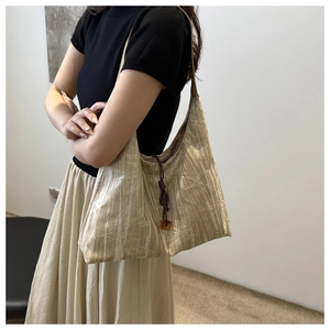 Detail of champagne gold pleated tote bag with amber charm and brown rope accents
