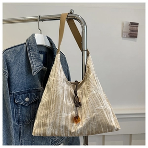 Close-up of pleated tote bag with plant prints, brown strap and dark wood pendant detail