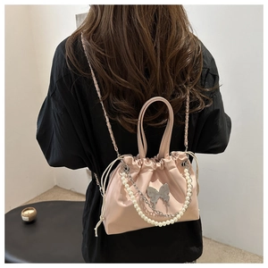 Détail du sac seau en satin rose avec chaîne de perles et breloque papillon en métal