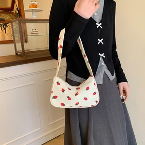 Witte corduroy hobo-tas met aardbeienprint gedragen door model in een knus café
