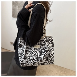 Close-up of zebra pattern canvas tote bag with leather logo tag and gold chain strap