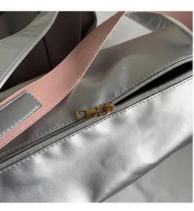 Primer plano de un bolso tote plateado metalizado con cremallera dorada y correa de cuero rosa