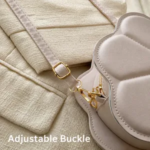 Close-up of adjustable metal buckle on cream crossbody bag with flower stitch patterns