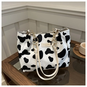 Detail view of the black and white cow print canvas tote bag with beige straps and gold chains