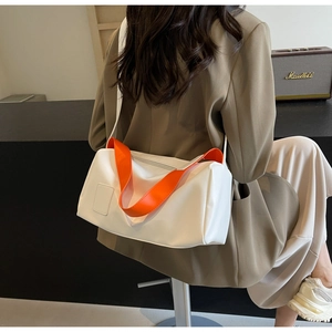 Detalle del bolso cilíndrico blanco con asas naranjas y correa ancha usado por una modelo