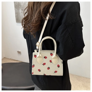 Detail der Cord-Handtasche mit Erdbeermuster und verstellbarem Gurt am Modell