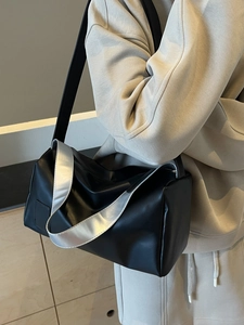 Minimalist black cylinder tote bag with silver decorative strap worn on shoulder