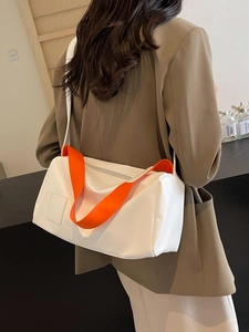 Minimalist white leather tote bag with contrast orange strap worn over a brown blazer