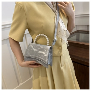 Dettaglio della mini borsa argento con manico di perle e texture metallica con base curva