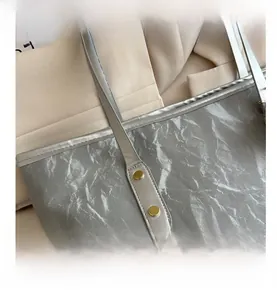 Détail du sac cabas argenté montrant la texture plissée et les rivets dorés