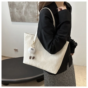 Détail d'un grand sac cabas blanc cassé avec un charme en peluche et texture en cuir