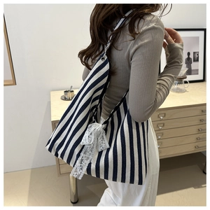 Detail einer blau gestreiften Canvas-Tasche mit weißer Spitzenschleife im Alltag
