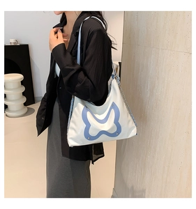 Detail of white tote bag featuring blue butterfly pattern and metal chain strap