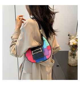 Close-up of rainbow patchwork crescent bag featuring a black leather flap and gold buckle