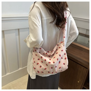 Détail du sac bandoulière en velours rose avec imprimé fraise porté par un modèle