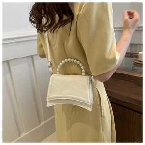 Dettaglio della borsa beige con manico di perle, trama lucida plissettata e tracolla