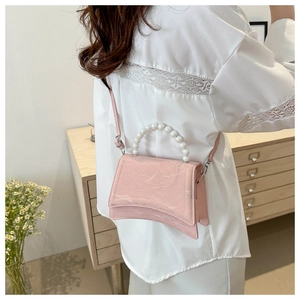 Dettaglio borsa con texture marmo rosa e manico di perle su un mobile in legno