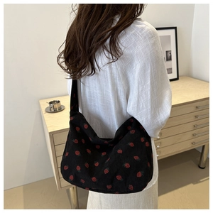 Détail d'un sac cabas en velours côtelé noir à motif fraise porté par un mannequin