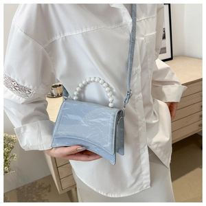 Dettaglio borsa celeste in pelle verniciata con manico di perle e base ricurva dal design unico