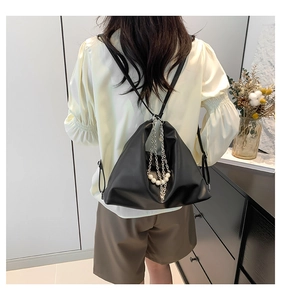 Detail of black faux leather tote with pearl and silver chain accents on model