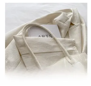 Detail of cream white tote bag with knot handle texture on tweed blazer and arts book