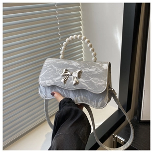 Detail of silver metallic textured crossbody bag with pearl handle and bow decoration