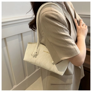 Detail of a creamy white underarm bag with pleated texture and gold lettering logo