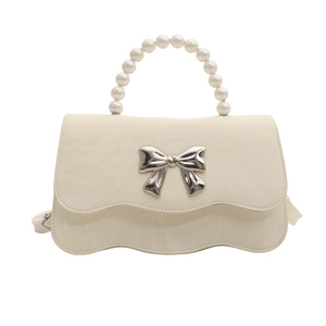 Cream bow handbag with pearl handle and metallic bow buckle in minimalist white background