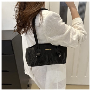 Detailed view of black pleated underarm bag with knotted strap and gold logo on model
