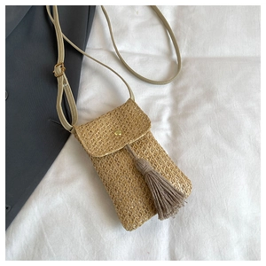 Detailed shot of straw woven phone bag featuring a long tassel and gold metal buckle