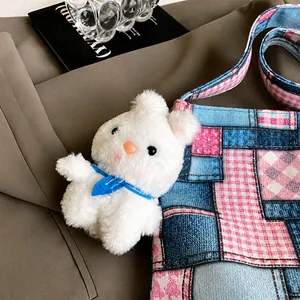 Gros plan d'un lapin en peluche blanc avec écharpe bleue attaché à un sac à carreaux
