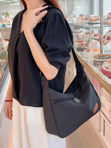 Black crescent nylon crossbody bag worn by model, featuring minimalist fashion style