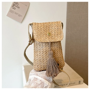 Detail of hand-woven straw phone bag with tassel fringe and golden metal buckle clasp