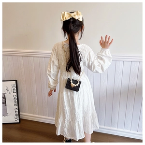 Détail d'un sac à bandoulière noir pailleté avec chaîne de perles sur robe blanche