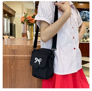 Close-up of black crossbody bag with a white bow detail shown in a cafe setting
