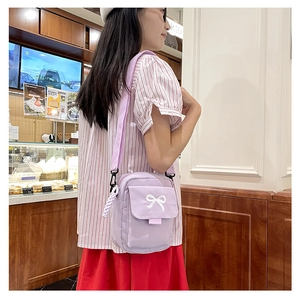 Lavender purple mini crossbody bag with white bow embroidery shown in a cafe setting