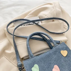 Detail of blue denim handbag featuring colorful heart patches and adjustable shoulder strap