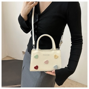 Detail of cream mini crossbody bag featuring colorful heart patches and fashion text