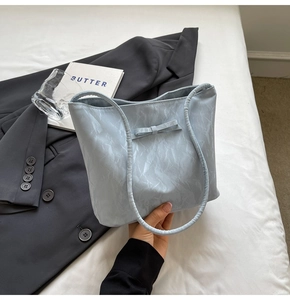Détail d'un sac cabas bleu clair en similicuir plissé avec petit nœud et deux poignées