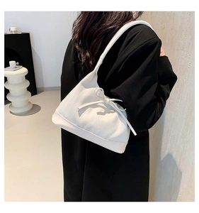 Model view of cream shoulder bag with wave texture and knot detail over black blazer