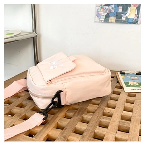 Detailed view of pink nylon crossbody bag with adjustable strap on a wooden tray