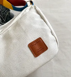 Détail du sac en toile blanche avec patch en cuir marron et bandoulière tissée colorée