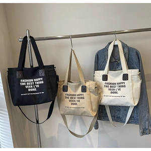 Three large canvas tote bags in black, khaki, and cream hanging on a metal display rack