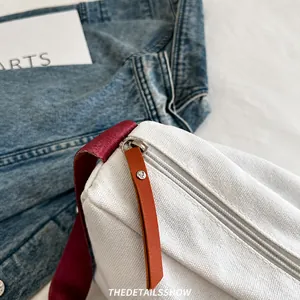 Détail du zip fluide sur un sac en toile blanc avec tirette en cuir et bandoulière rouge