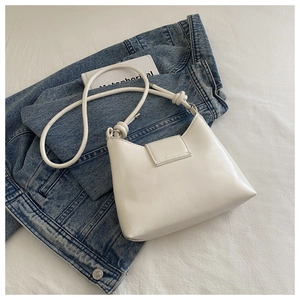Close-up of minimalist white PU leather shoulder bag with knot detail on denim background