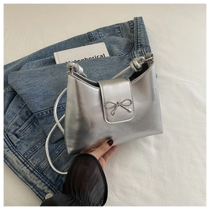Detail of silver metallic underarm bag with bow hardware and knotted strap design