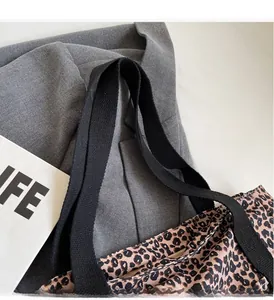 Close-up of leopard print canvas tote bag with black woven handles on a grey jacket