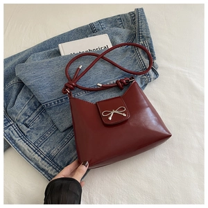 Detail of dark red patent leather shoulder bag featuring a silver bow and knotted strap