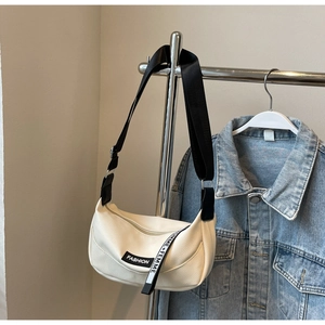 Détail d'un sac blanc à texture litchi avec large bandoulière noire et étiquette