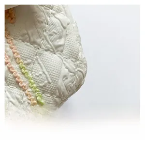 Détail d'un sac à main blanc matelassé avec bordure florale tissée et texture en losange